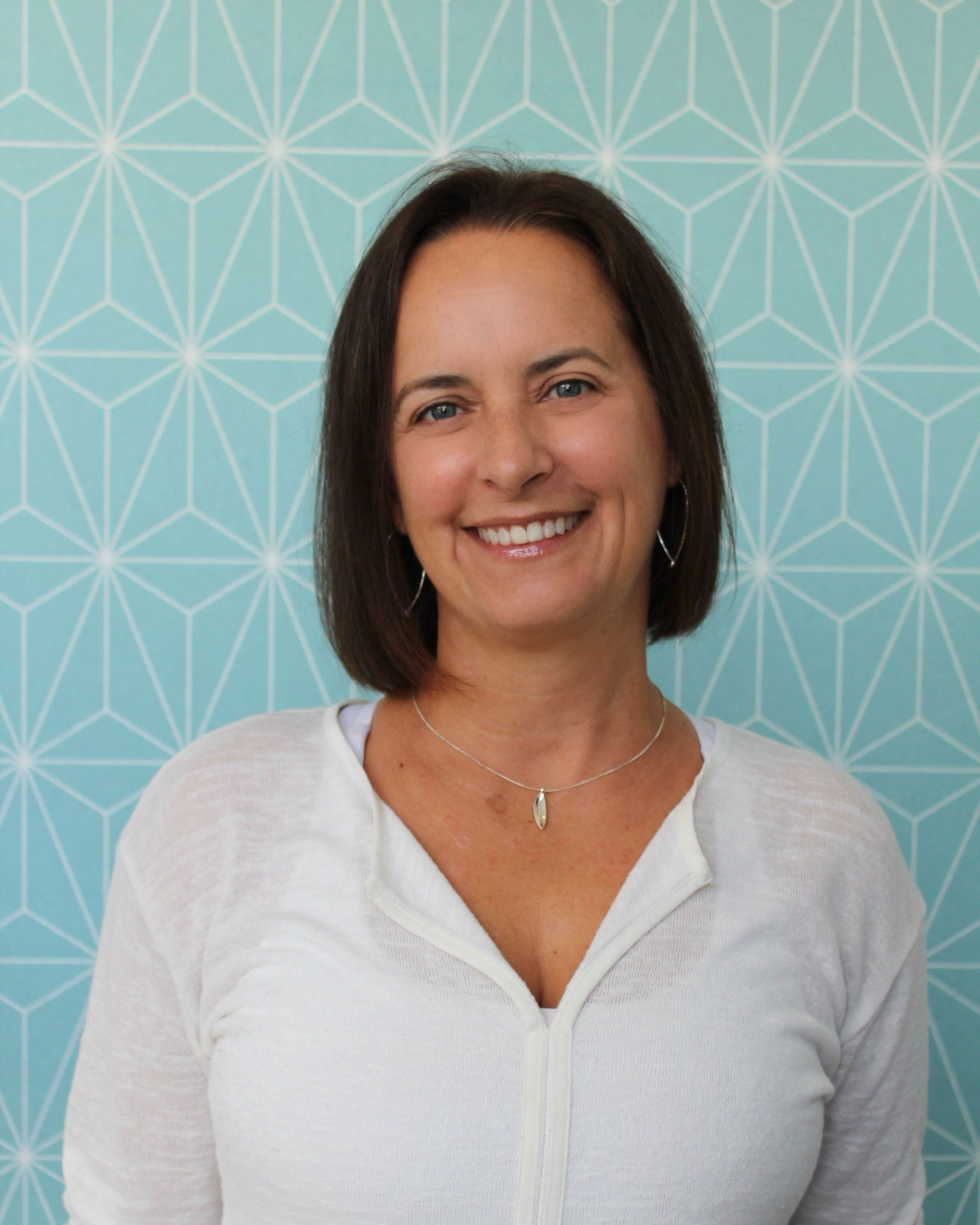 Louise Brans Fitzgibbon smiling in front of a pale blue geometric-patterned wall