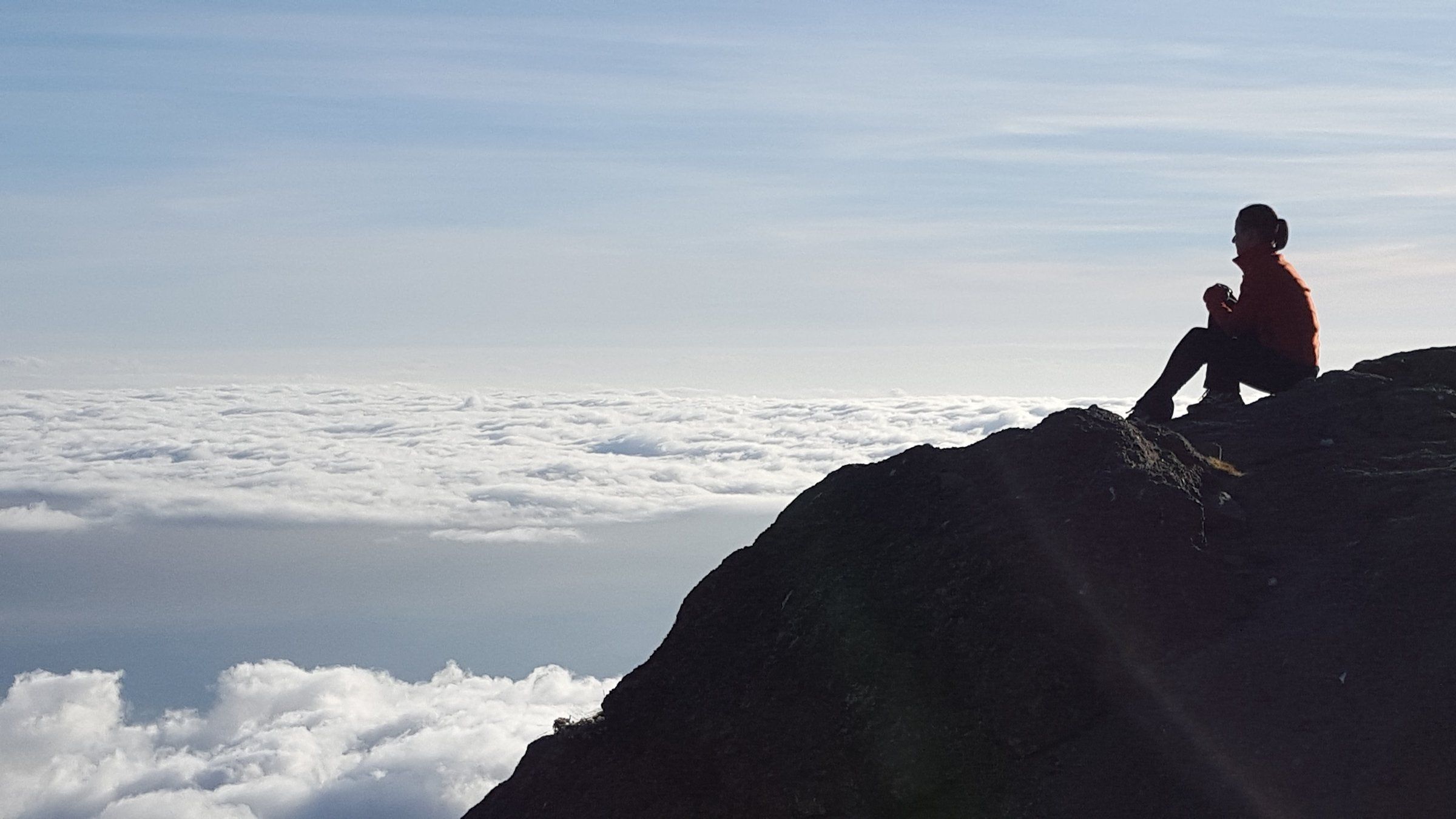 Louise seated on a rocky ridge on Mount Kilimanjaro, looking out over a sea of clouds