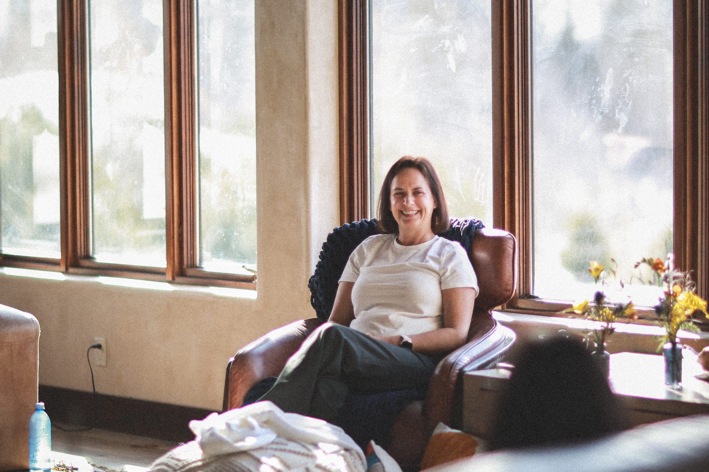 Louise laughing warmly in an armchair by a sunlit window wall